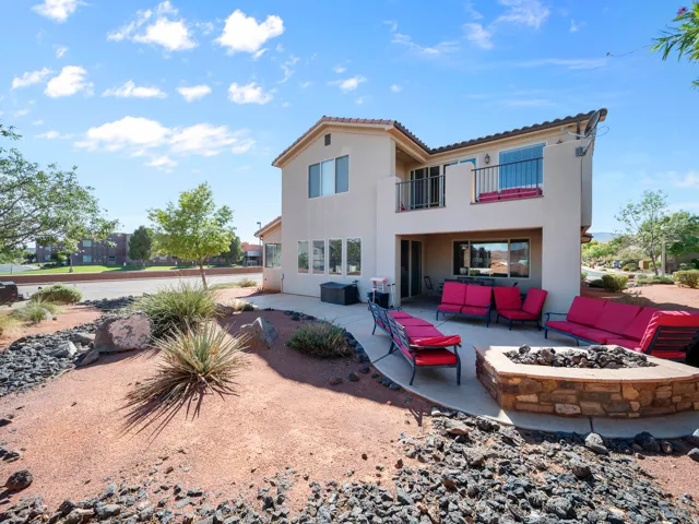 Stucco exterior with a tiled roof, featuring a ground-level patio, a stone-clad fire pit, and an upper-level balcony with metal railings