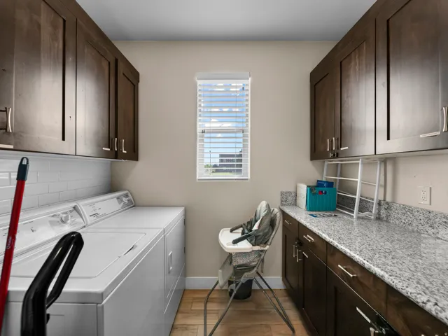 Laundry area featuring wood-finish flooring, white subway tile backsplash, dark wood cabinetry with silver-tone hardware, and a light-toned speckled countertop