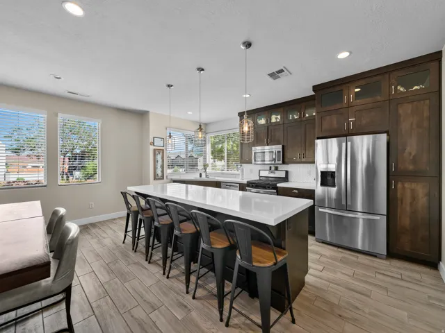 Spacious kitchen featuring an expansive island with seating, extensive dark wood cabinetry, integrated stainless steel appliances, modern pendant lighting, and wood-finish flooring