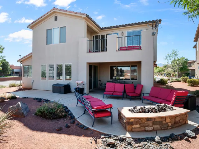 Upper-level balcony with metal railing, ground-level covered patio, and a stone-clad fire pit