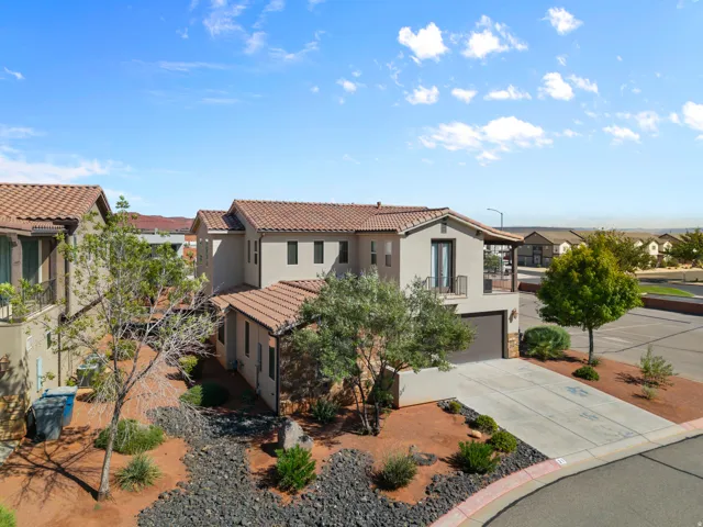 Mediterranean-inspired residence featuring a terracotta tile roof, stucco exterior with mixed finish materials, and a professionally designed front courtyard with hardscaped pathways, native drought-resistant landscaping, and mature specimen trees