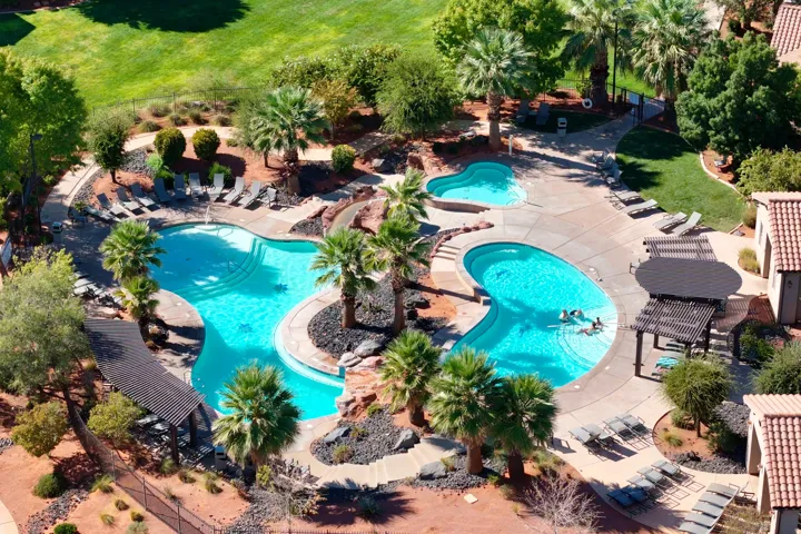 Multiple swimming pools, mature palm trees, integrated rock landscaping, sun loungers, and shaded pergola seating