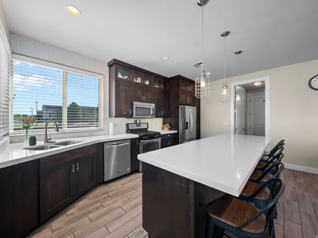Contemporary kitchen featuring dark wood cabinetry, white countertops, stainless steel appliances, and wood-finish flooring