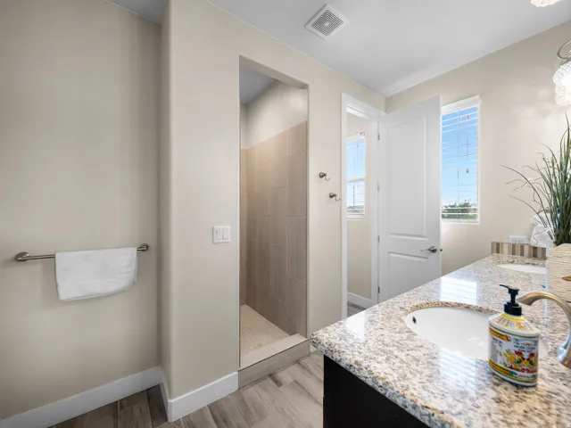 Walk-in shower with tiled surround and floor, dual sink vanity with stone countertop, and wood-finish flooring