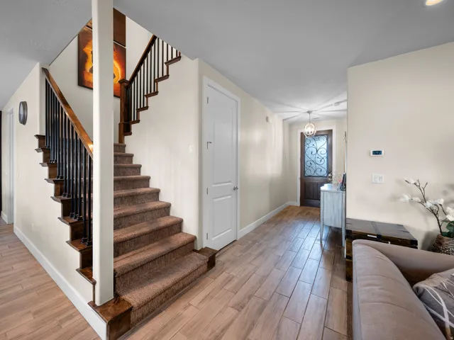 Wood-finish flooring, staircase with carpeted treads and dark wood handrails, wrought iron balusters, white interior doors, and a decorative front entry door with obscure glass