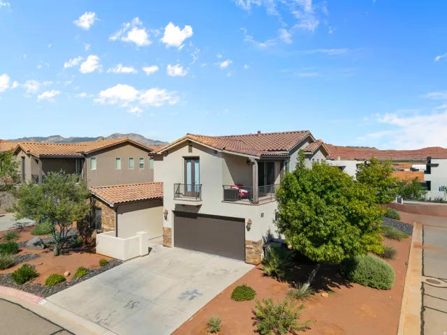 Stucco exterior with stone accents, tile roofing, an attached garage, and upper-level balconies