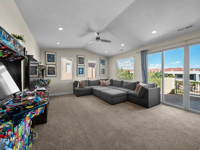 Vaulted ceiling with recessed lighting, ceiling fan, carpeted flooring, multiple windows with blinds, and sliding glass door access to an exterior balcony