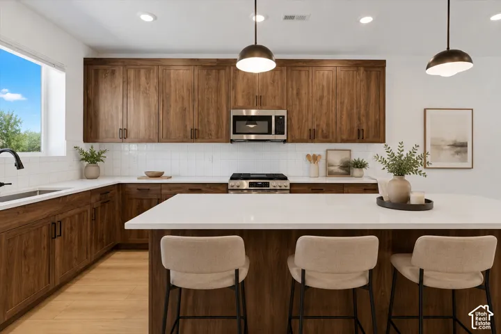 Kitchen featuring wood-finish cabinetry, white subway tile backsplash, white countertops, and stainless steel appliances