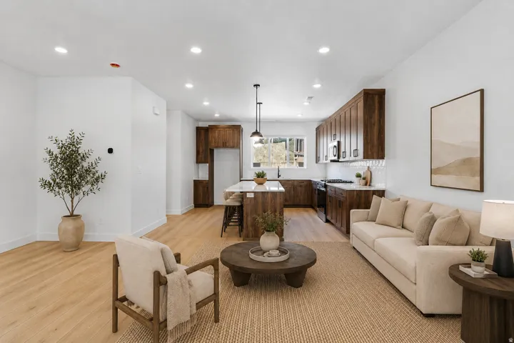 Open-concept living space with wood-finish flooring, recessed lighting, a kitchen island with seating, a tile backsplash, and dark wood cabinetry