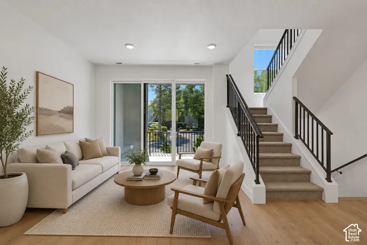 Wood-finish flooring, white walls, recessed lighting, sliding glass door, and a staircase with carpeted treads and black metal railings