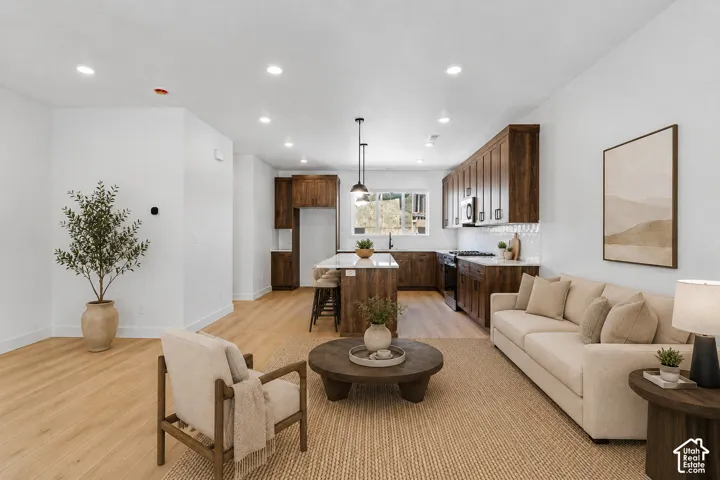 Open-concept living space with wood-finish flooring, recessed lighting, a kitchen island with seating, a tile backsplash, and dark wood cabinetry