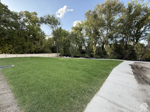 Expansive green lawn with a defined concrete pathway, bordered by a substantial privacy fence and mature trees