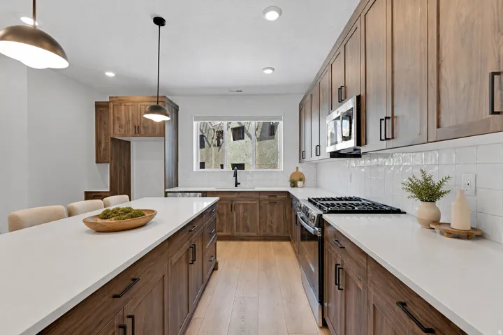 Kitchen featuring wood-finish cabinetry, white countertops, tile backsplash, stainless steel appliances, and a central island