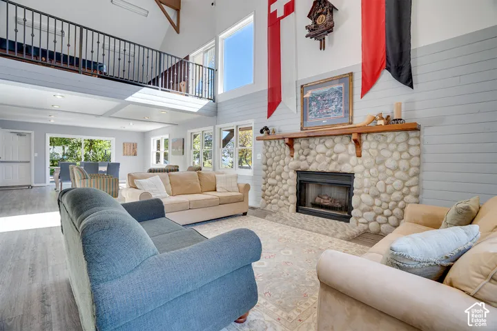 Vaulted ceiling with exposed wood beams, river rock fireplace with wood mantel, horizontal plank wall paneling, and metal spindle railing overlooking the living area
