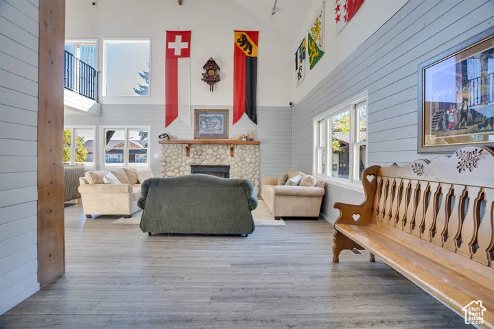 Vaulted ceiling, stone fireplace with a wood mantel, horizontal paneled walls, wood-finish flooring, and multi-pane windows