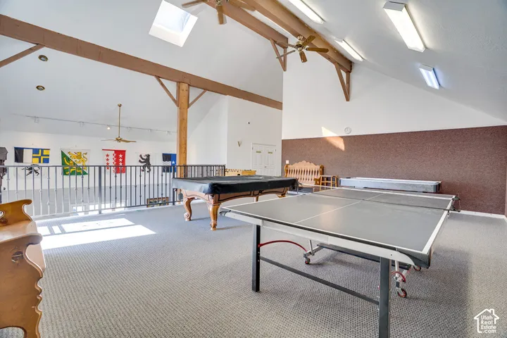 Vaulted ceiling featuring exposed timber beams, skylights, track lighting, and ceiling fans, complemented by a metal railing