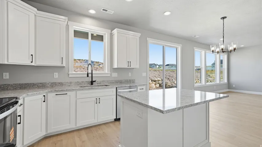White cabinetry with black hardware, light-toned wood-finish flooring, and a central island with a light-toned countertop