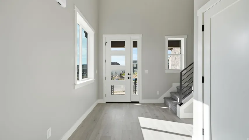 Entryway with wood-finish flooring, a white paneled entry door with multiple lites, a matching sidelite, a window, and a staircase with a black metal railing