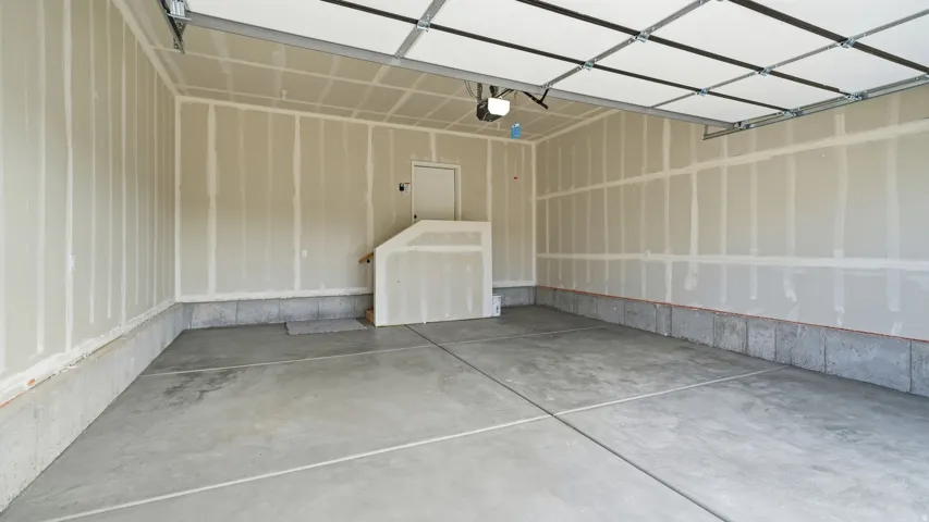Concrete flooring, unfinished drywall, overhead garage door, built-in staircase, and an interior door