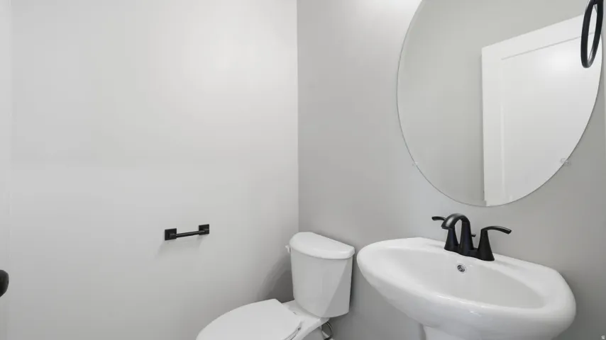 Pedestal sink with a matte black faucet, wall-mounted circular mirror, and neutral wall paint