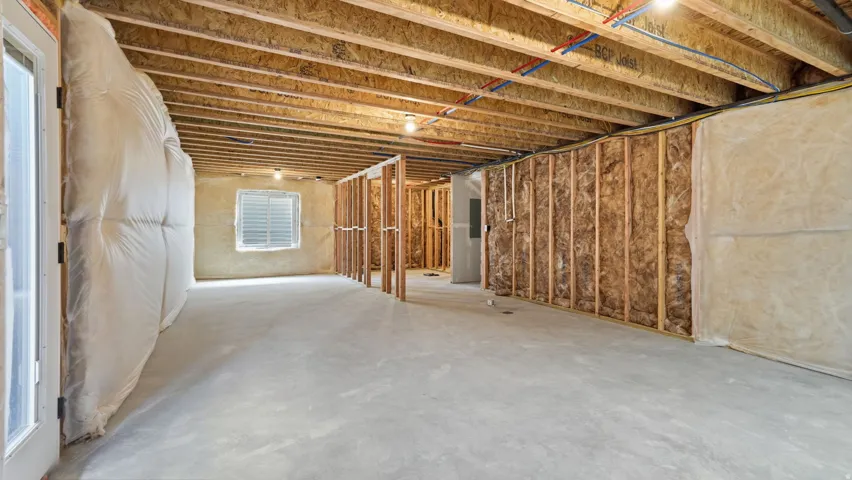 Unfinished basement with exposed ceiling joists, concrete flooring, framed wall sections, and a window with horizontal blinds