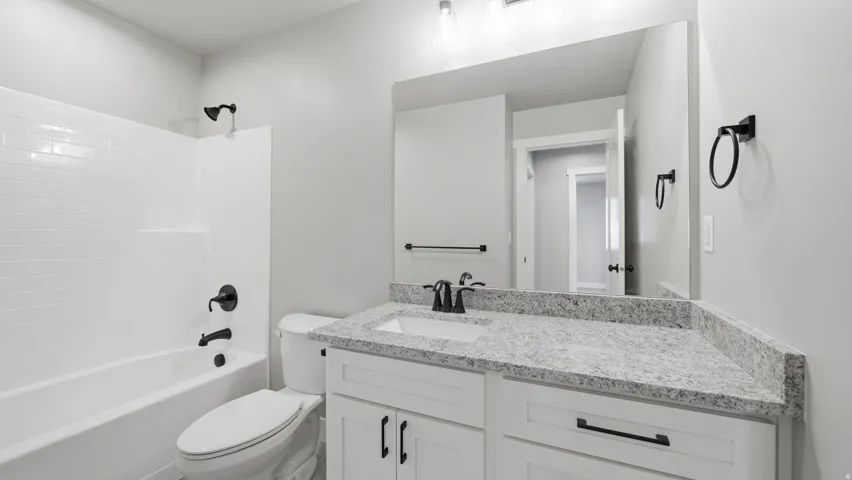 Bathroom featuring a white subway tile shower surround, matte black fixtures, a white vanity with shaker-style cabinetry, and a speckled countertop