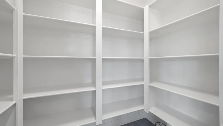 Walk-in pantry featuring extensive white shelving and dark wood-finish flooring