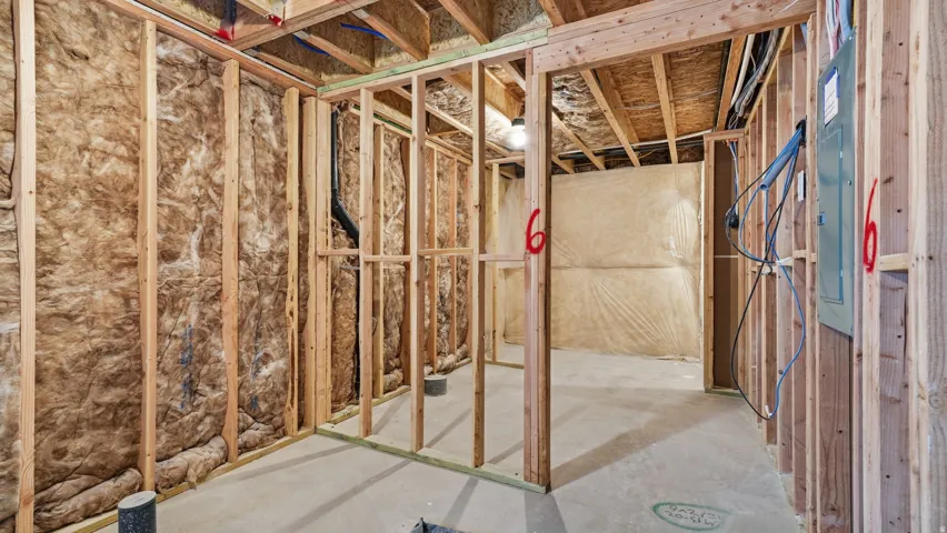 Unfinished basement featuring wood framing, insulation, concrete flooring, exposed ceiling joists, and an electrical panel