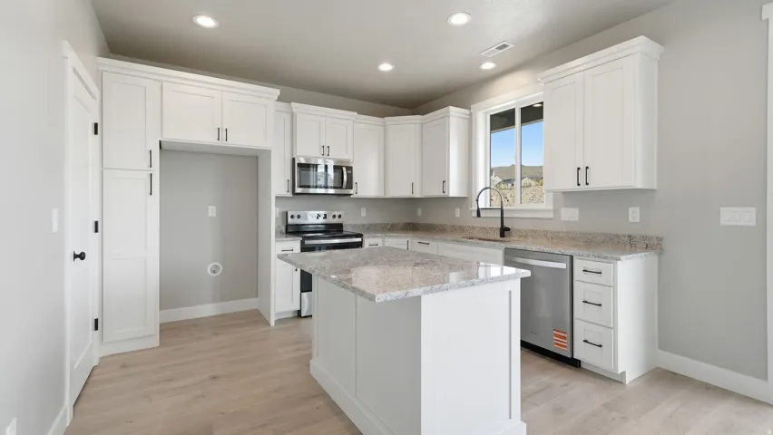 Kitchen featuring white cabinetry, light-toned wood-finish flooring, recessed lighting, stainless steel appliances, and a central island with a light-colored countertop