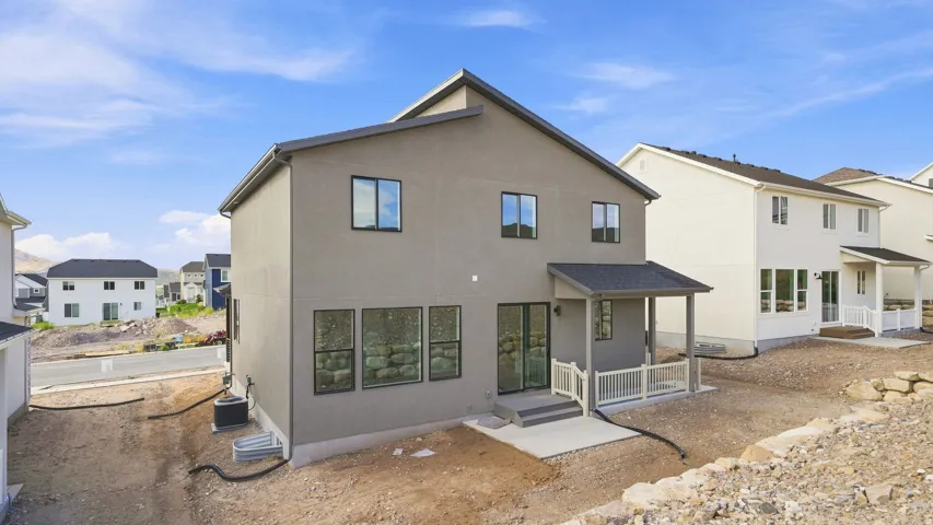 Stucco exterior with a covered patio, white railing, and a ground-level concrete pad