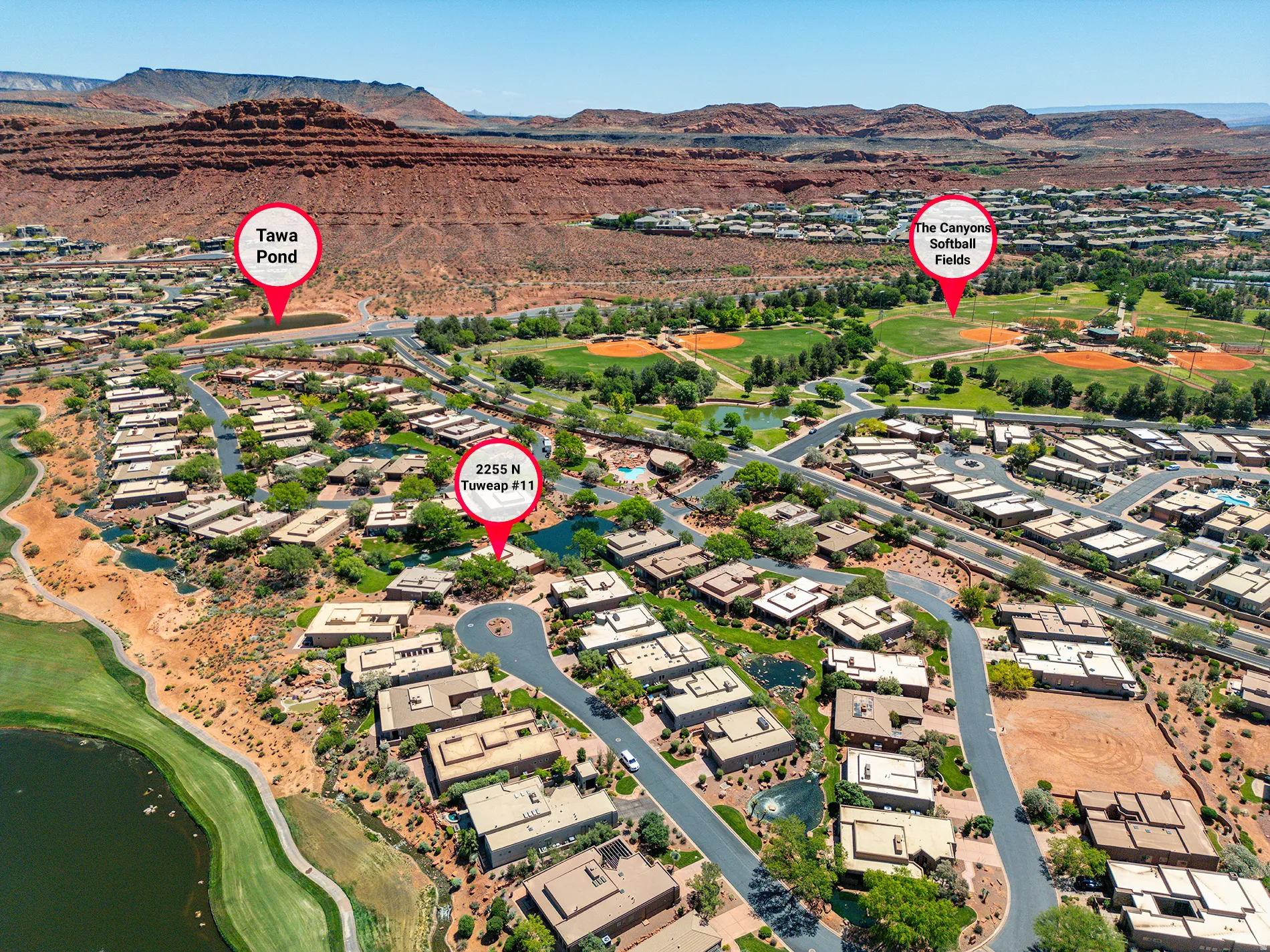 Aerial overview featuring a residential community, surrounding red rock formations, and green recreational areas