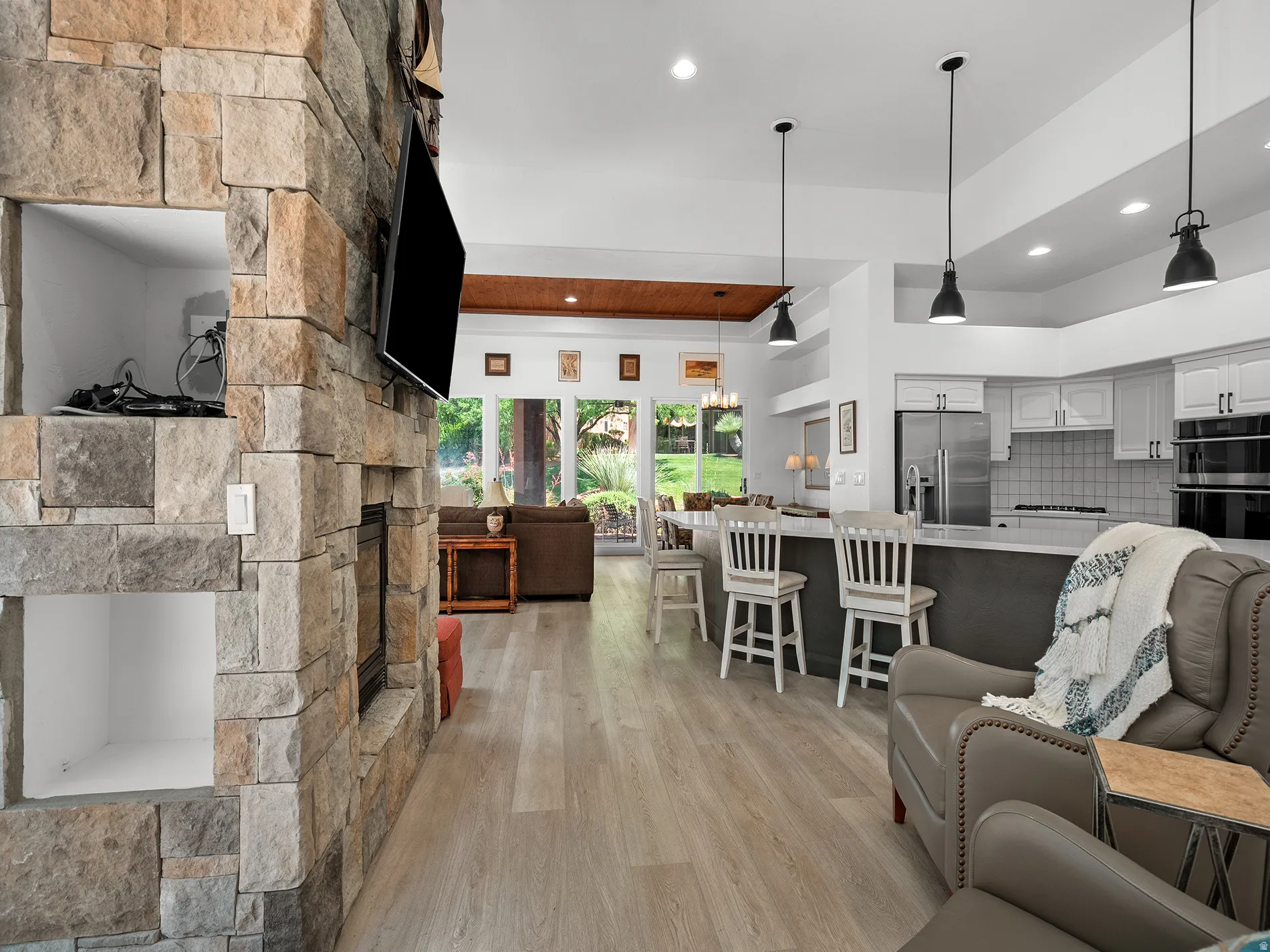 Stone-clad fireplace with built-in niches, light wood-finish flooring, recessed lighting, kitchen island with seating, and white cabinetry