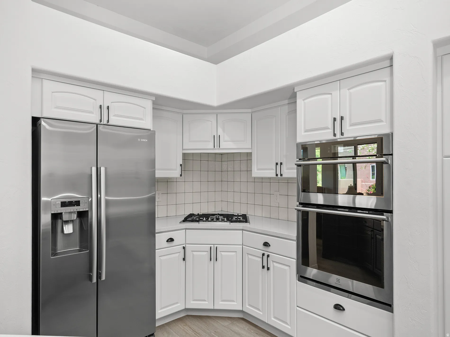 White cabinetry with dark hardware, stainless steel side-by-side refrigerator, gas cooktop, double wall ovens, and light-toned backsplash