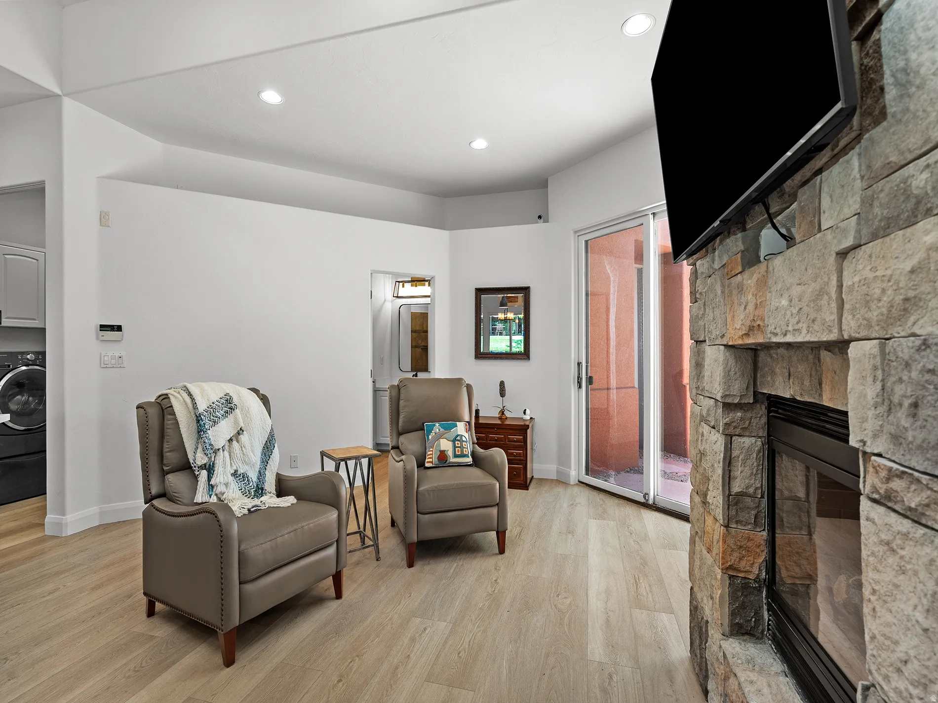 Stone-clad fireplace with a built-in firebox, sliding glass door, recessed lighting, and wood-finish flooring