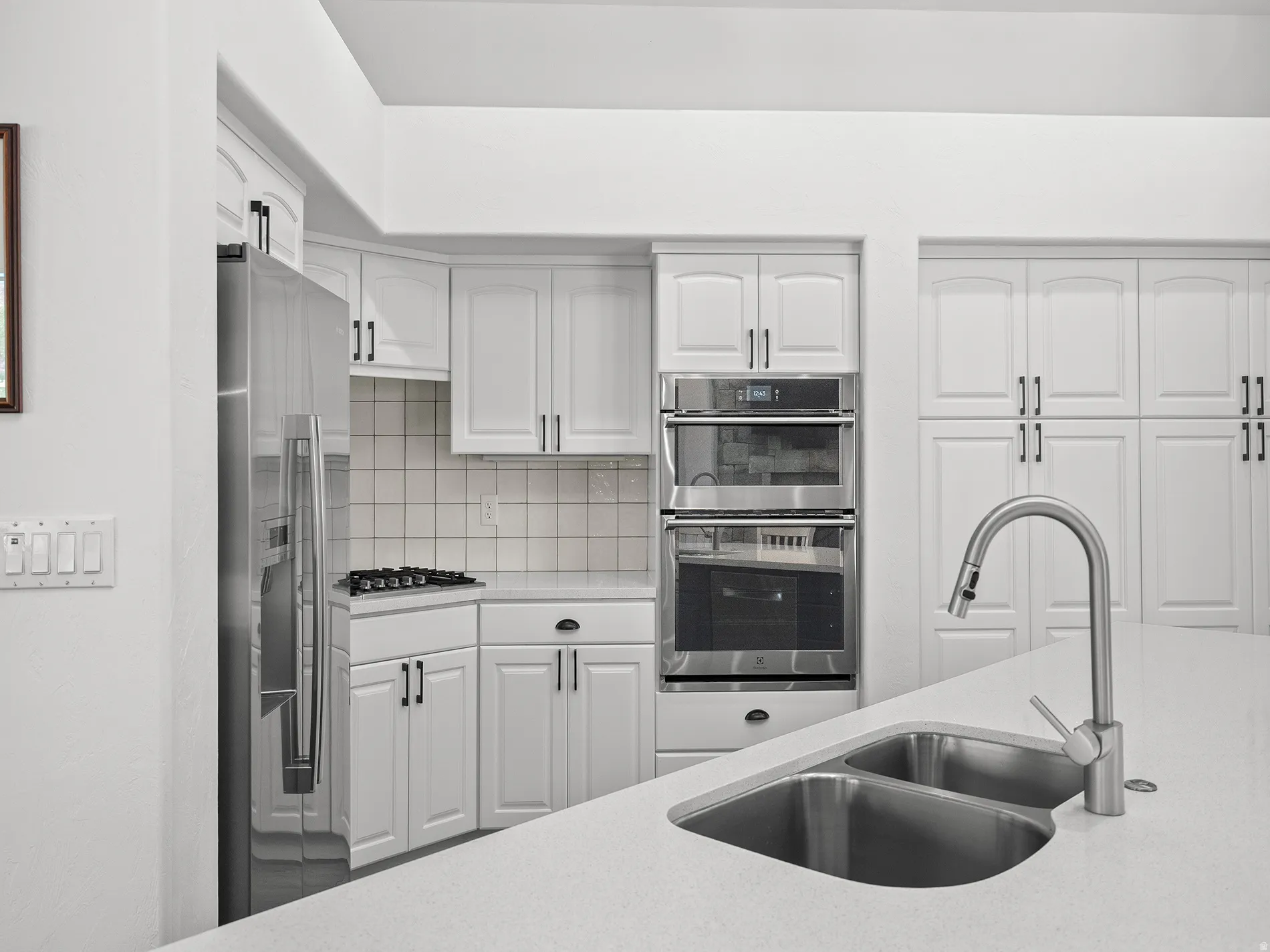 Modern kitchen with white cabinetry, stainless steel appliances, double basin sink, and solid surface countertops