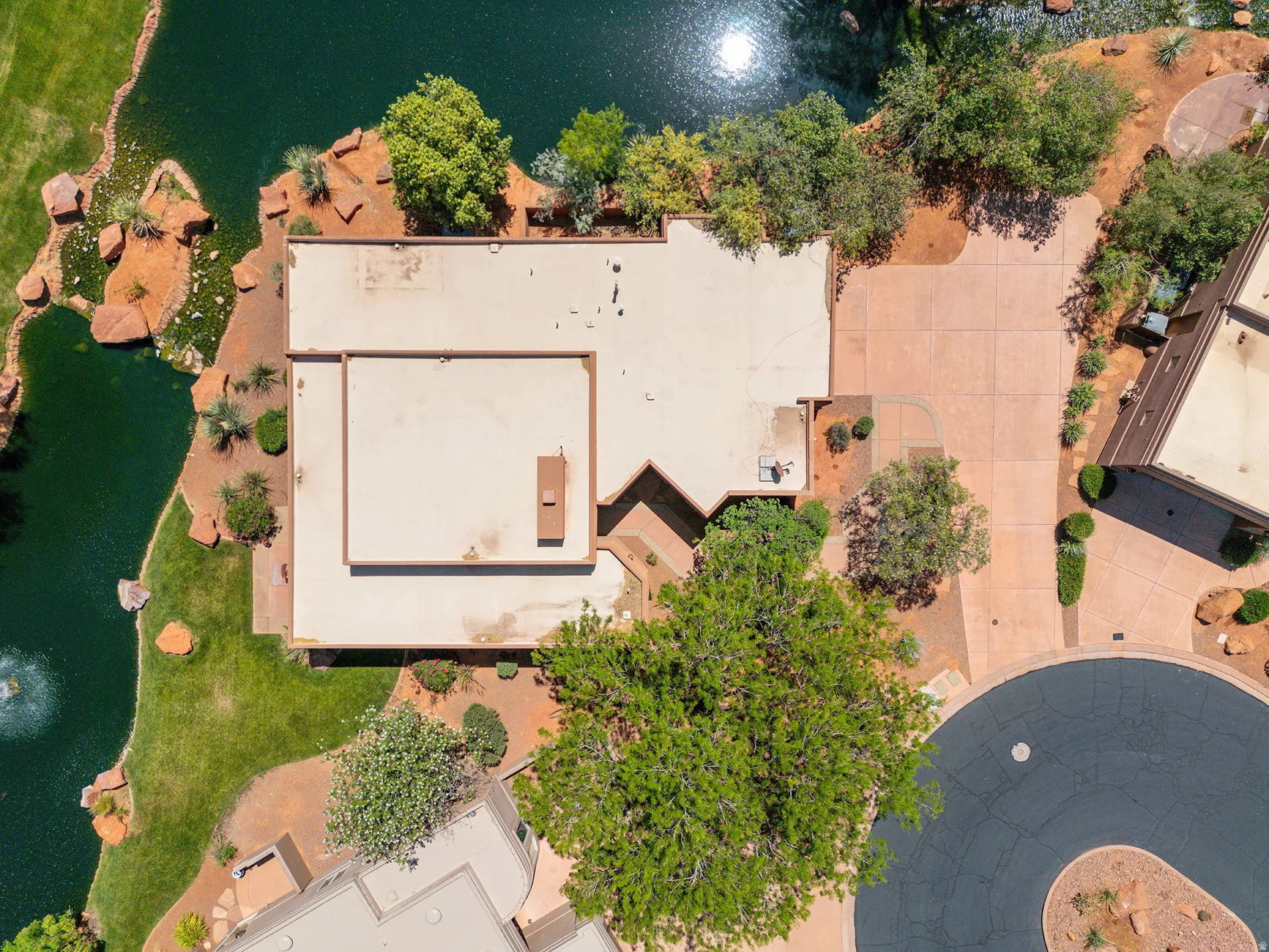 Property featuring a flat roofline, extensive paved driveway, mature trees, and a water feature