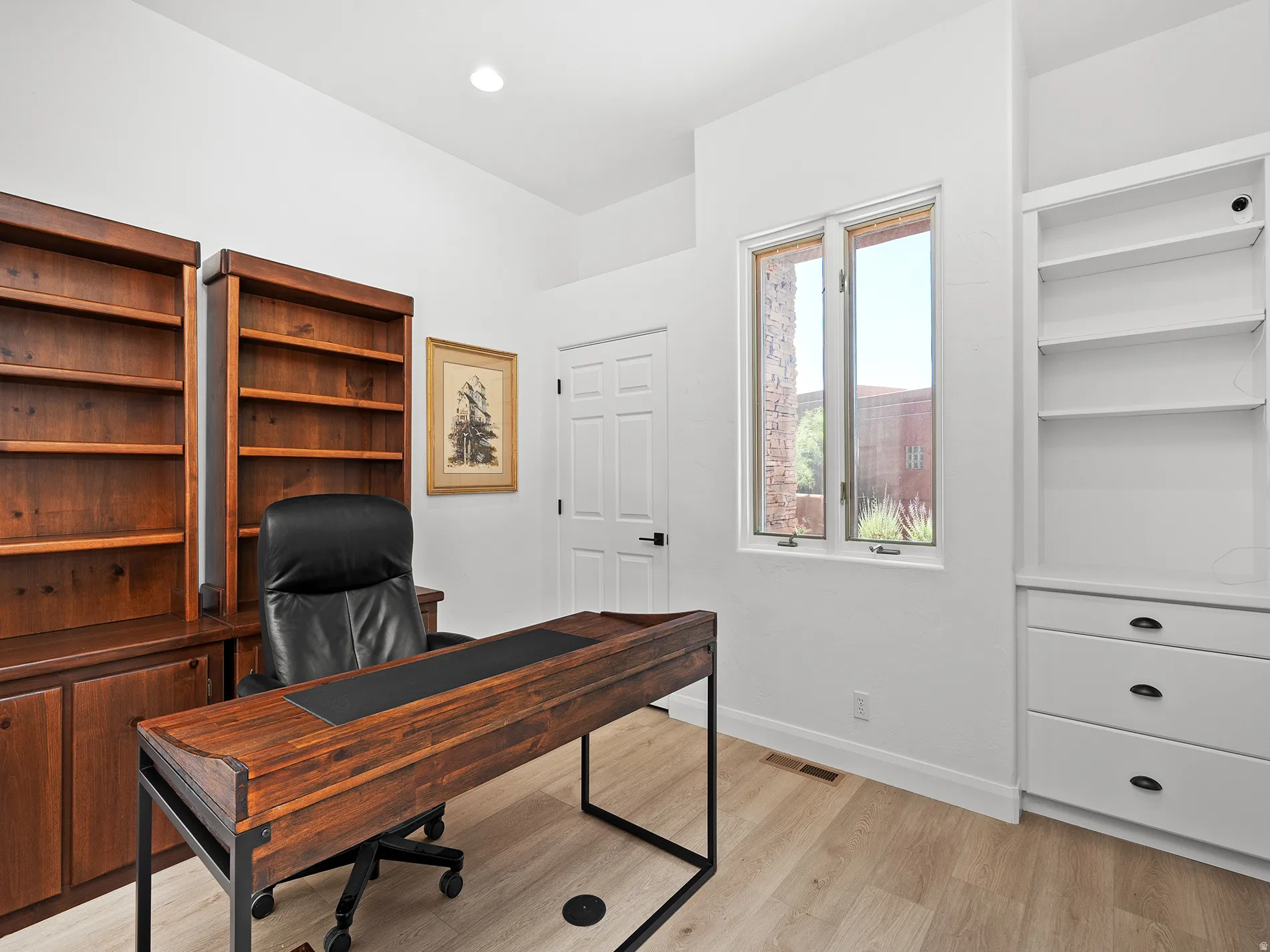 Built-in wood-finish shelving, built-in white cabinetry with drawers, neutral wall color, wood-finish flooring, and a single window