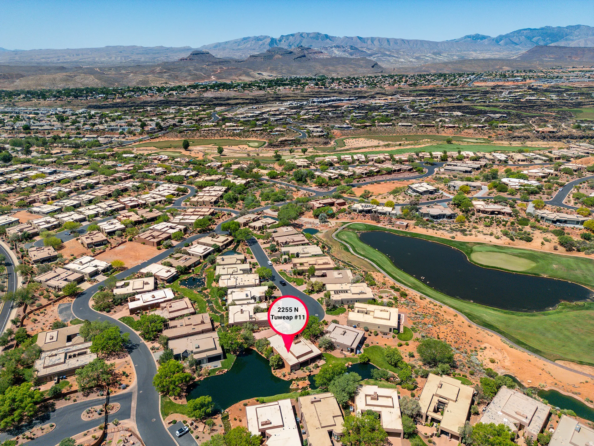 Aerial perspective showcasing a residential community with a large body of water, green golf course, and mountain range backdrop