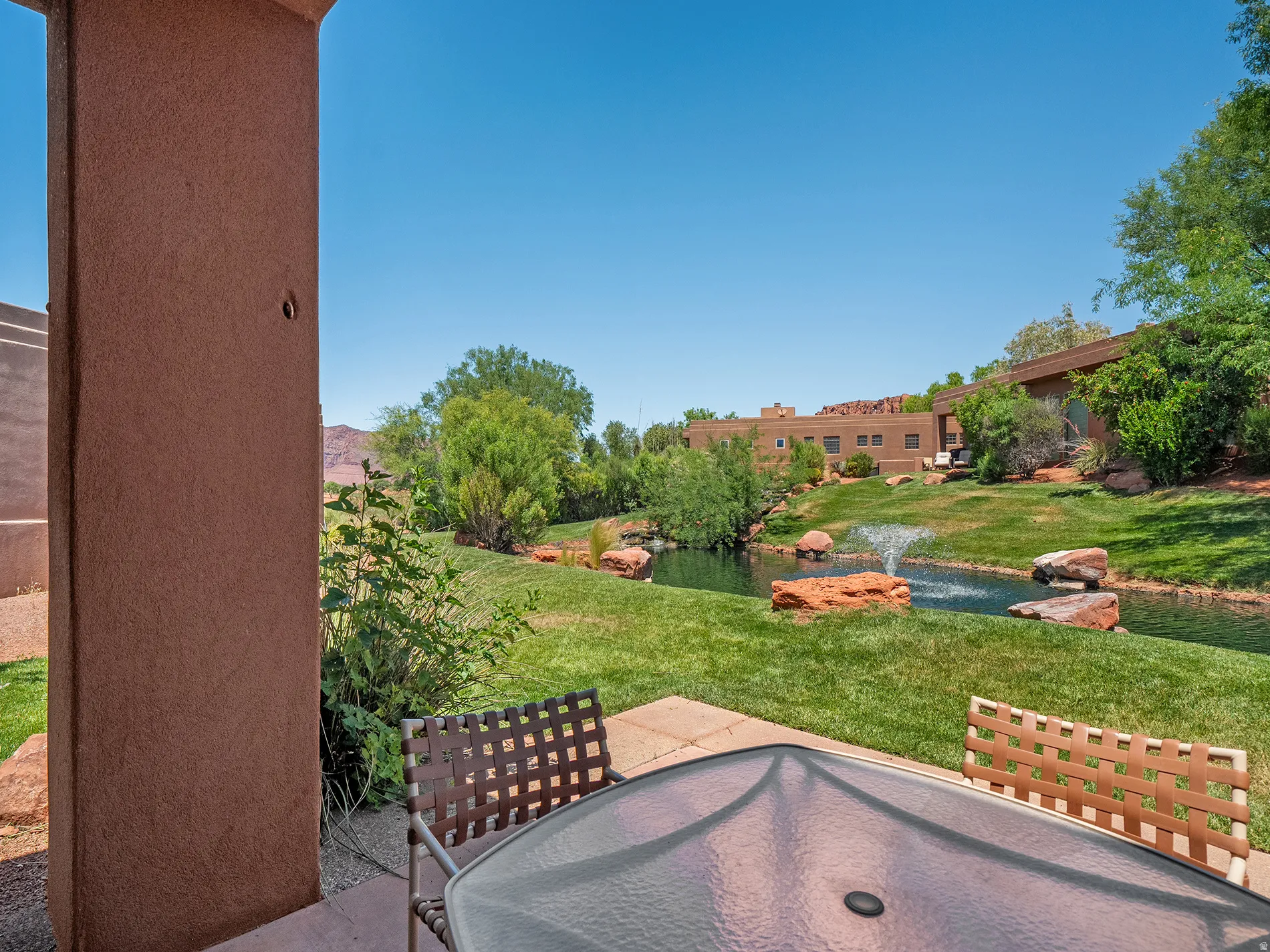 Patio with concrete flooring, stucco exterior wall, and direct access to a water feature with a fountain, surrounded by green landscaping