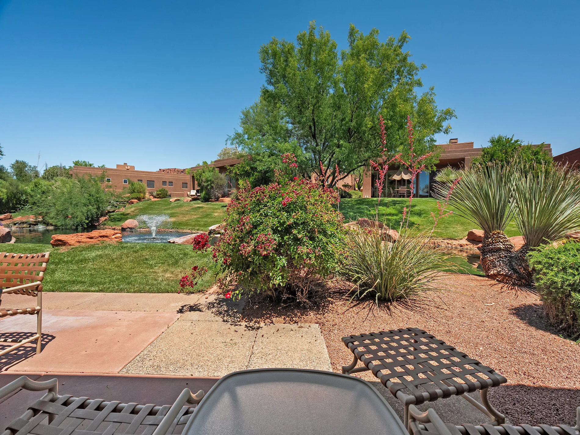 Patio area featuring a stone and concrete surface, landscaped yard with mature trees, shrubbery, and a water feature with a fountain