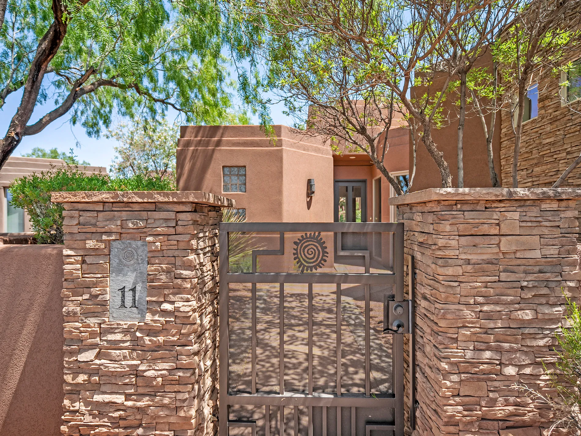 Stucco exterior featuring stacked stone accents, decorative iron gate, and mature trees