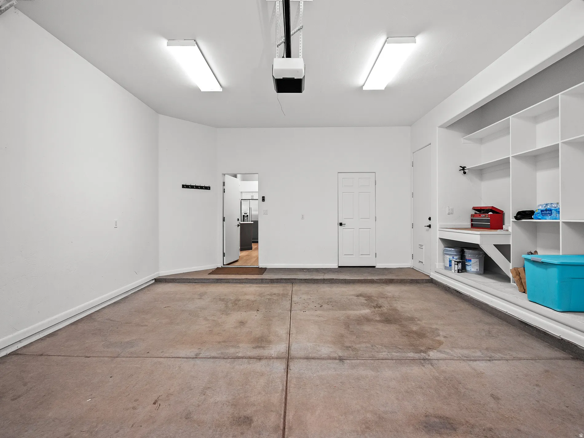 Attached garage with concrete flooring, built-in shelving, workbench, and overhead fluorescent lighting