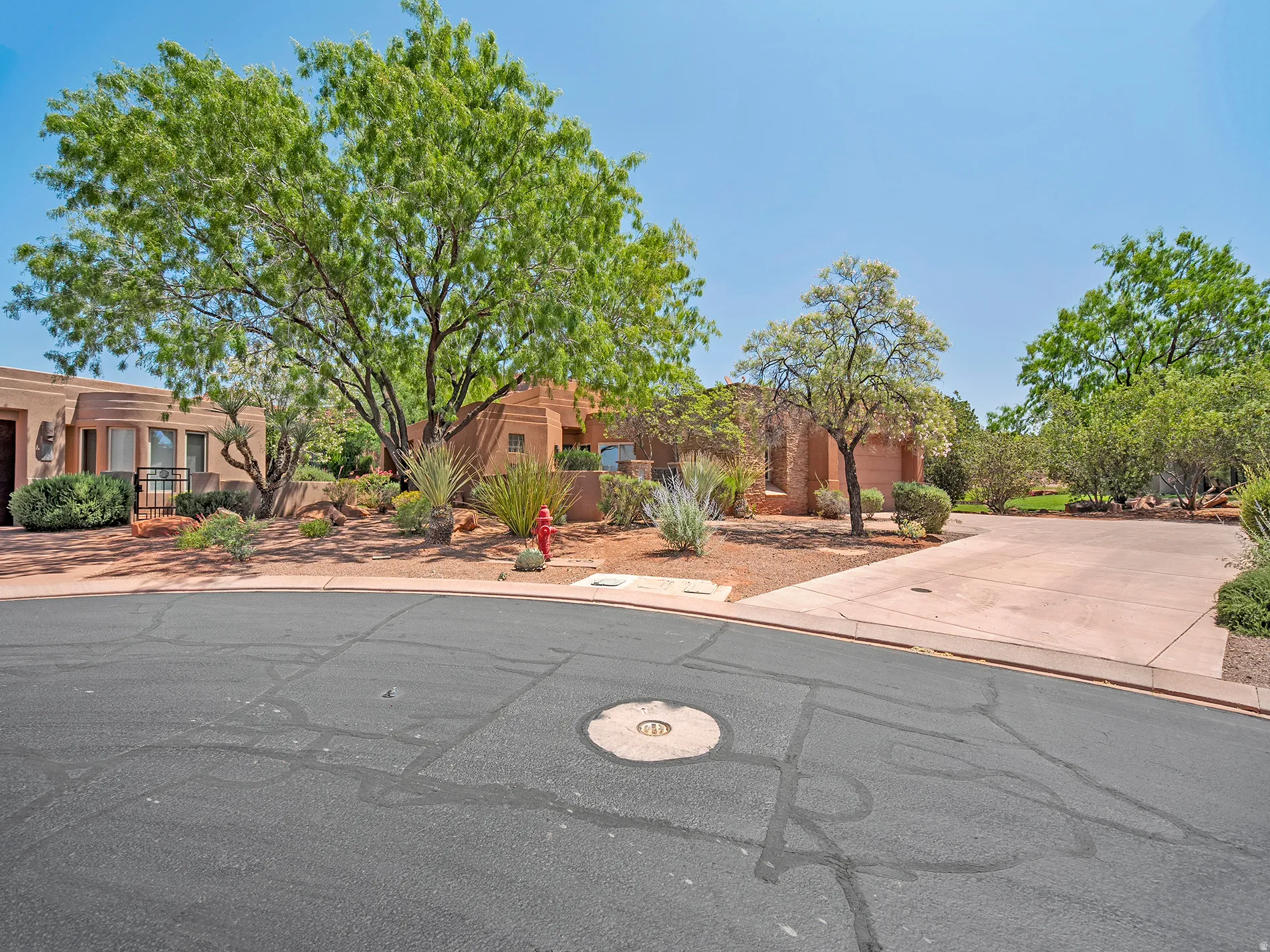Stucco exterior with mature trees, desert landscaping, and an attached garage