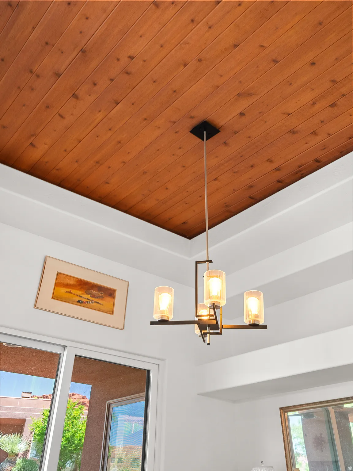 Wood-paneled ceiling with a contemporary chandelier, featuring frosted glass shades and a dark metal frame