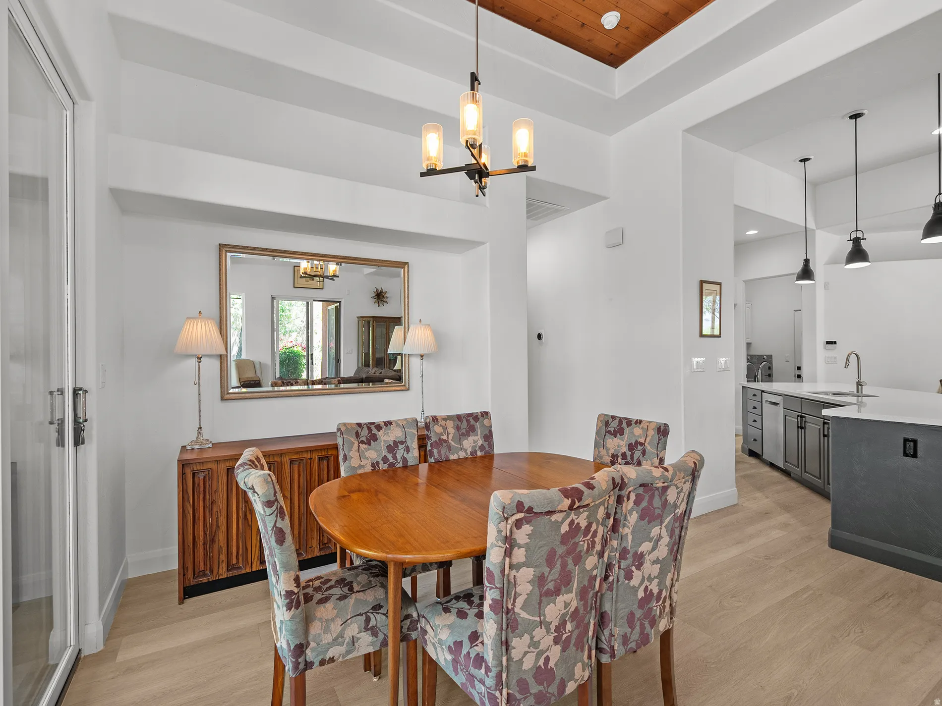 Tray ceiling with wood-paneled insert, wood-finish flooring, built-in display niche, and contemporary chandelier