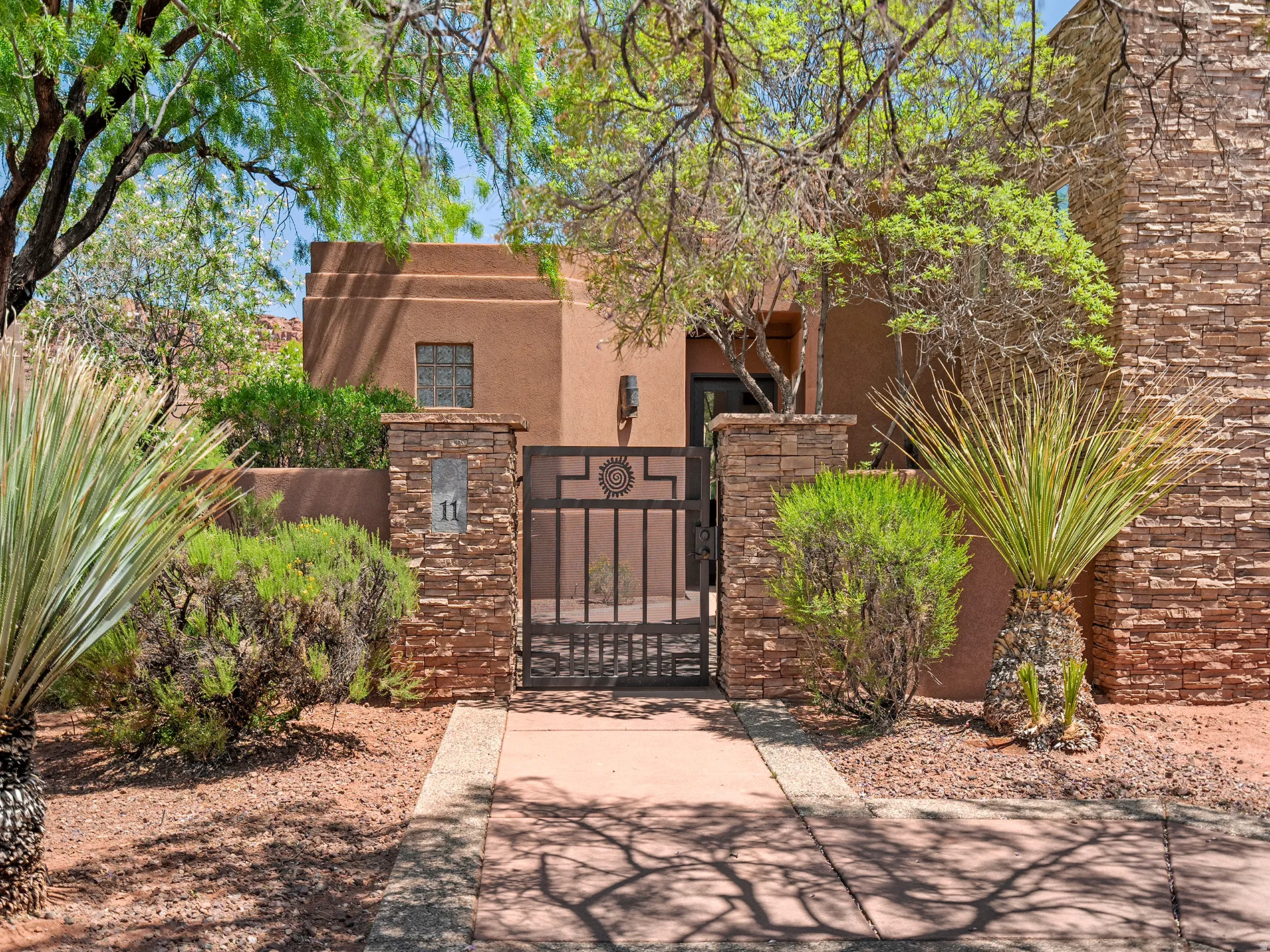 Stucco exterior with stone veneer accents, decorative wrought iron gate, paved walkway, and desert landscaping