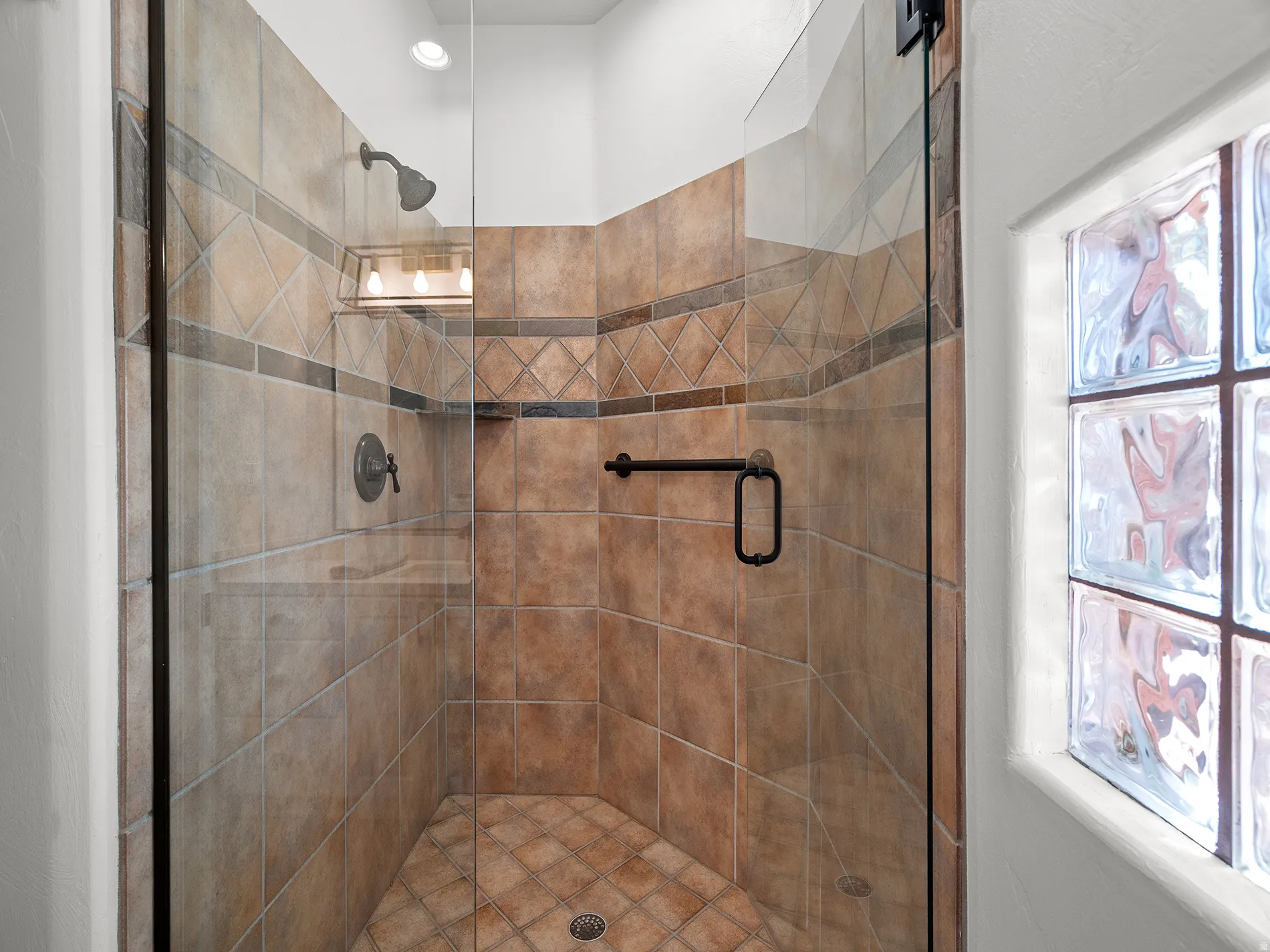 Glass-enclosed shower with tile surround and floor, featuring an integrated light fixture, showerhead, and wall-mounted faucet