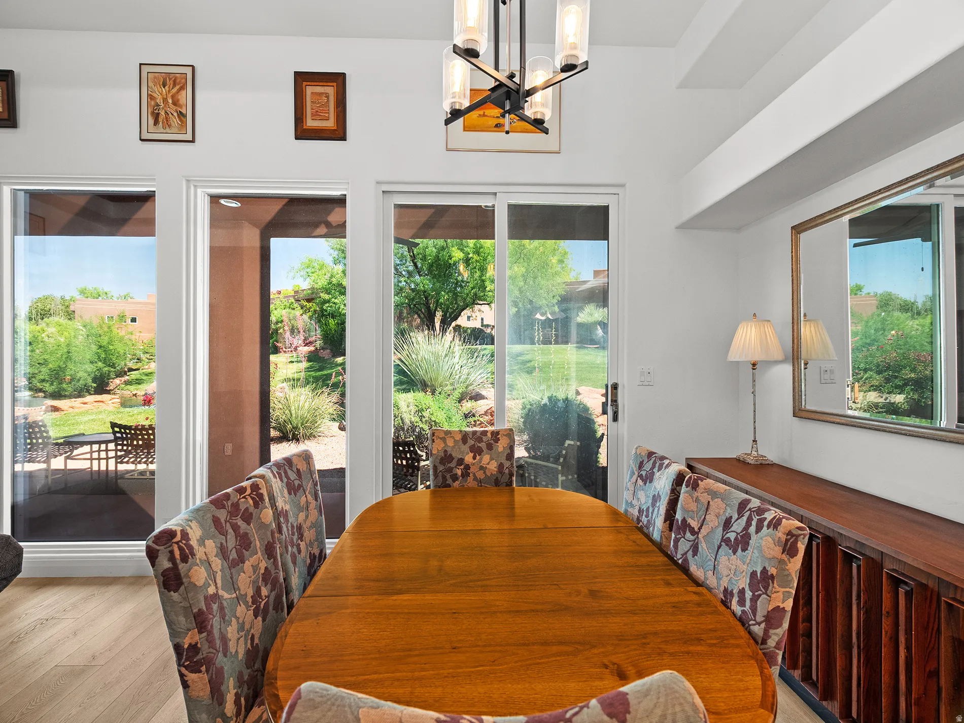 Spacious dining area with wood-finish flooring, a contemporary chandelier, abundant natural light from multiple windows, and a sliding glass door opening to outdoor living