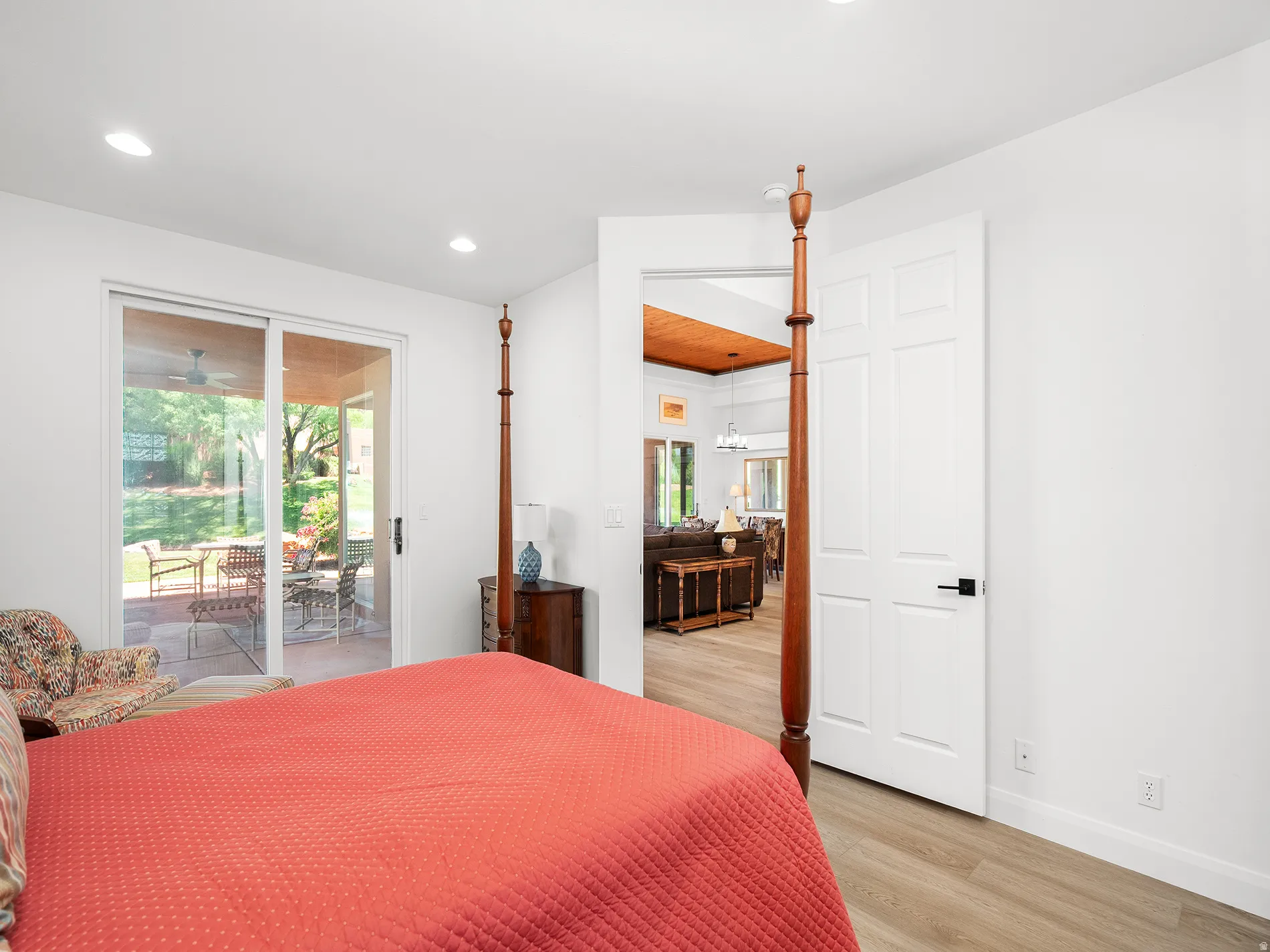 Recessed ceiling lighting, wood-finish flooring, white panel door with black hardware, sliding glass door, and a covered patio area with pavers