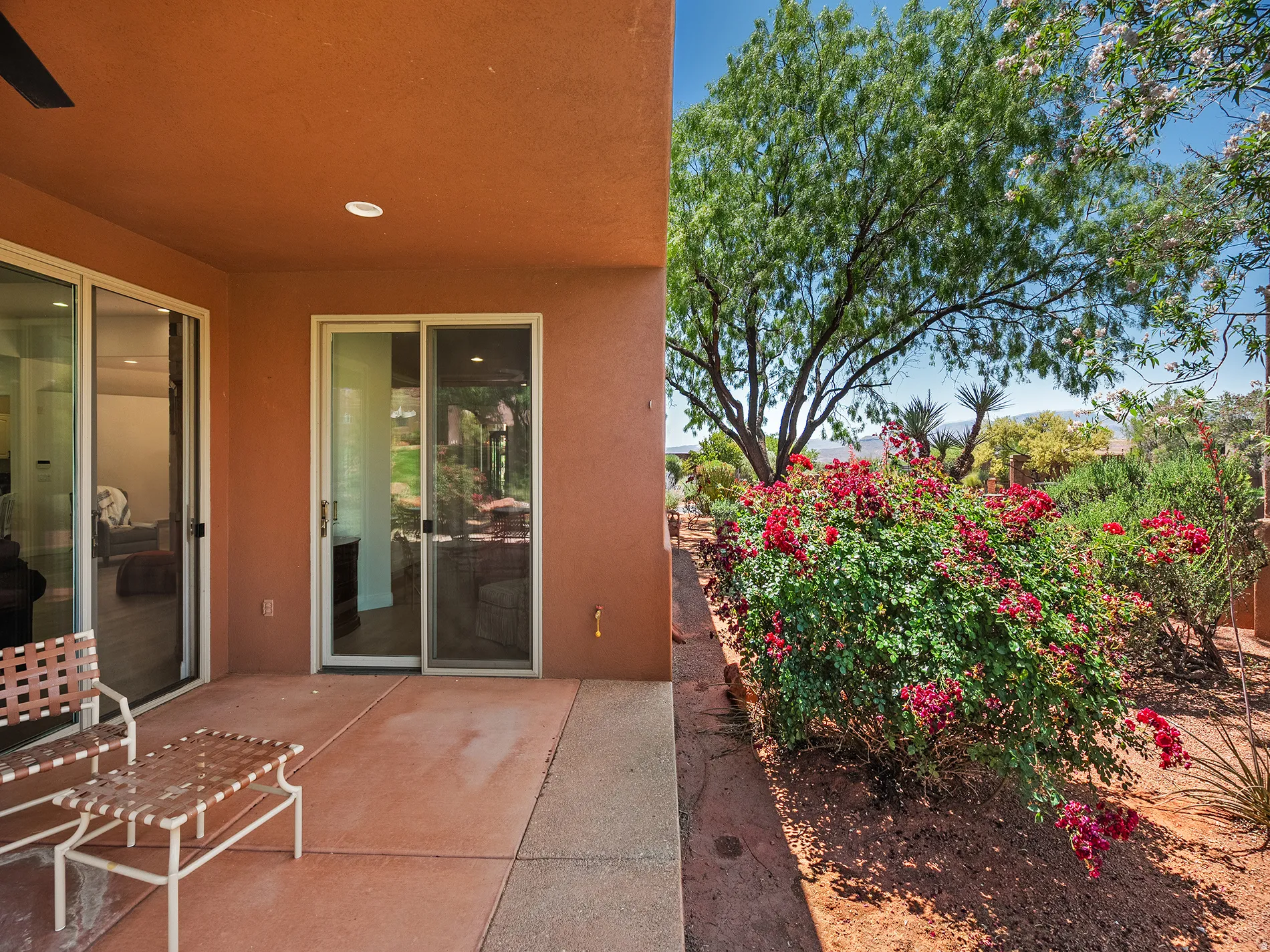 Private patio with two sets of sliding glass doors, recessed lighting, and a mature tree and shrubbery